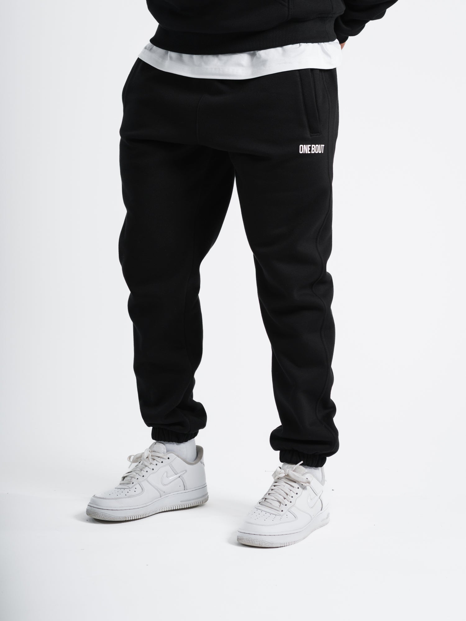 Male model wearing black ONE BOUT Script Bottoms with white sneakers